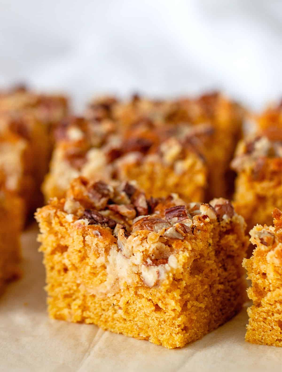 One main square of pecan topped pumpkin cake, others blurred in grey background