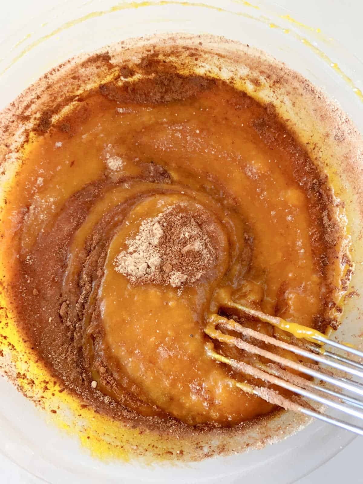 Mixing spices into pumpkin batter with a whisk.