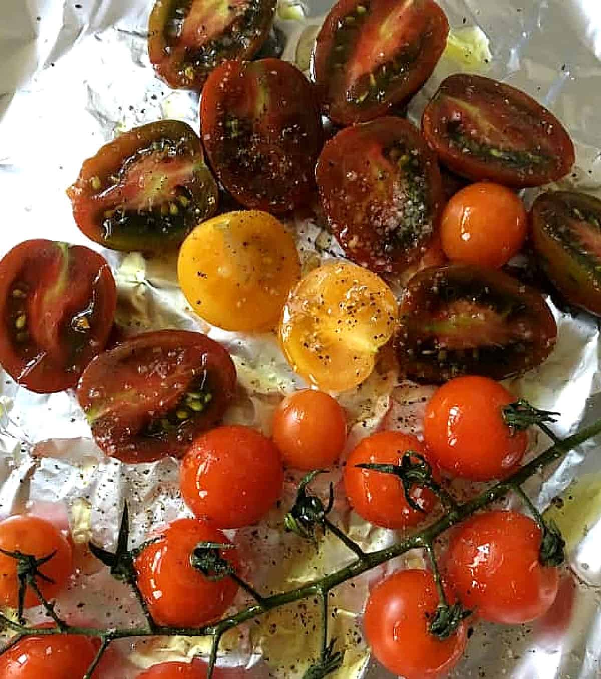 Halved and whole different colored cherry tomatoes on aluminum paper.