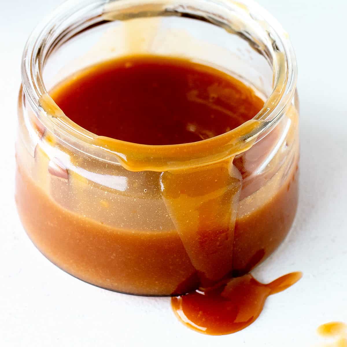 Close up of jar with dulce de leche on a white surface.