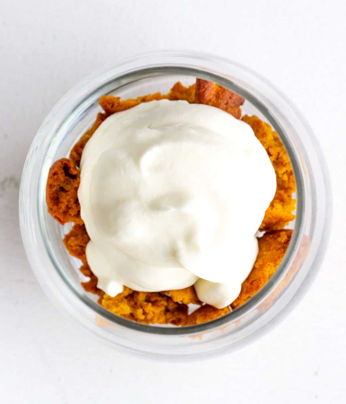 Top view of whipped cream dollop atop pumpkin cake crumbs in a glass.