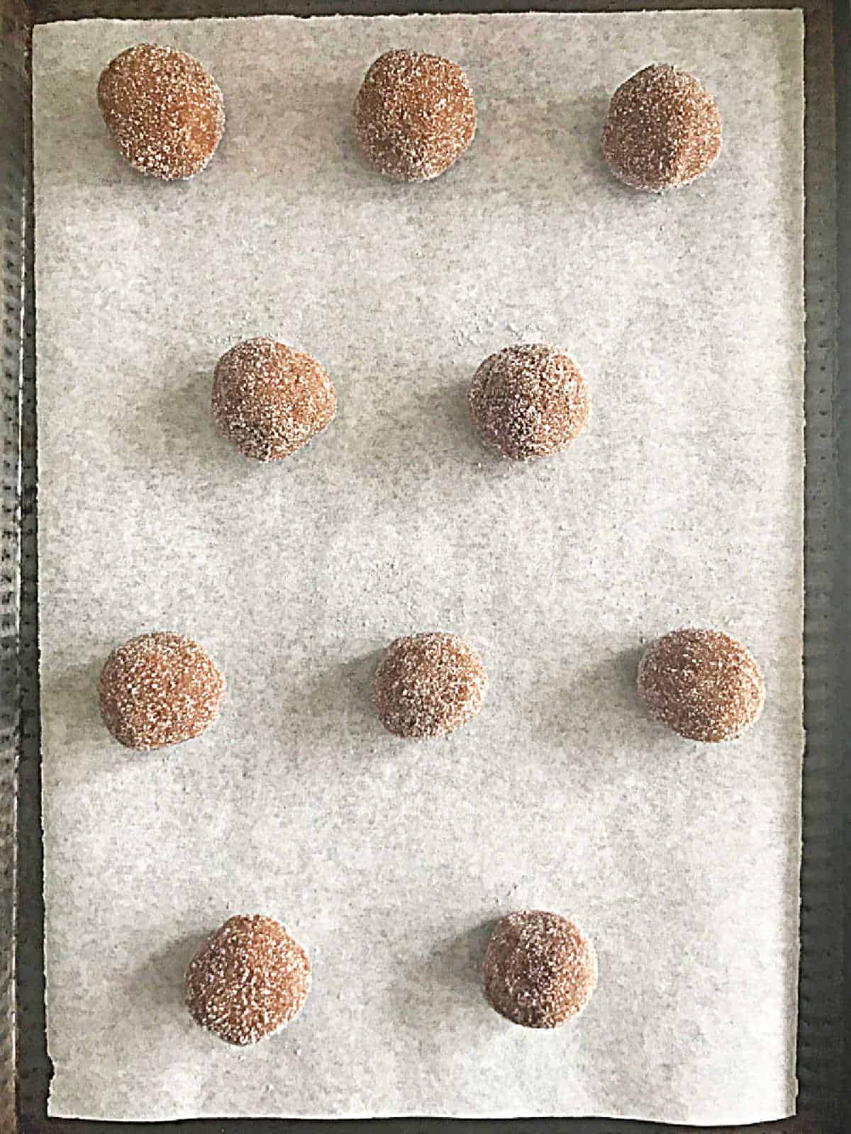 Cookie sheet with parchment paper and sugar-coated gingersnap dough balls. Top view.