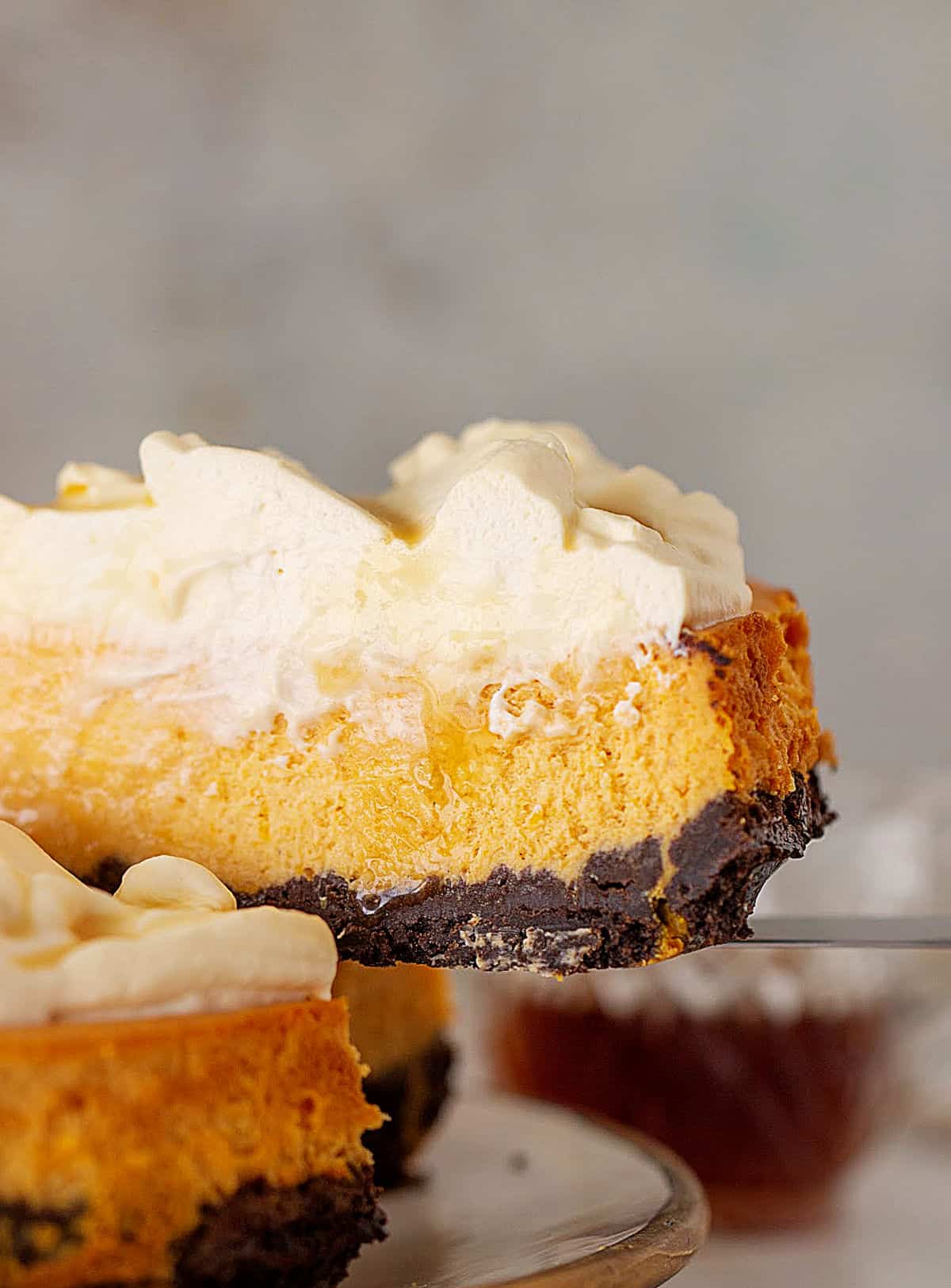 Partial slice of pumpkin cheesecake with whipped cream and chocolate crust, grey background