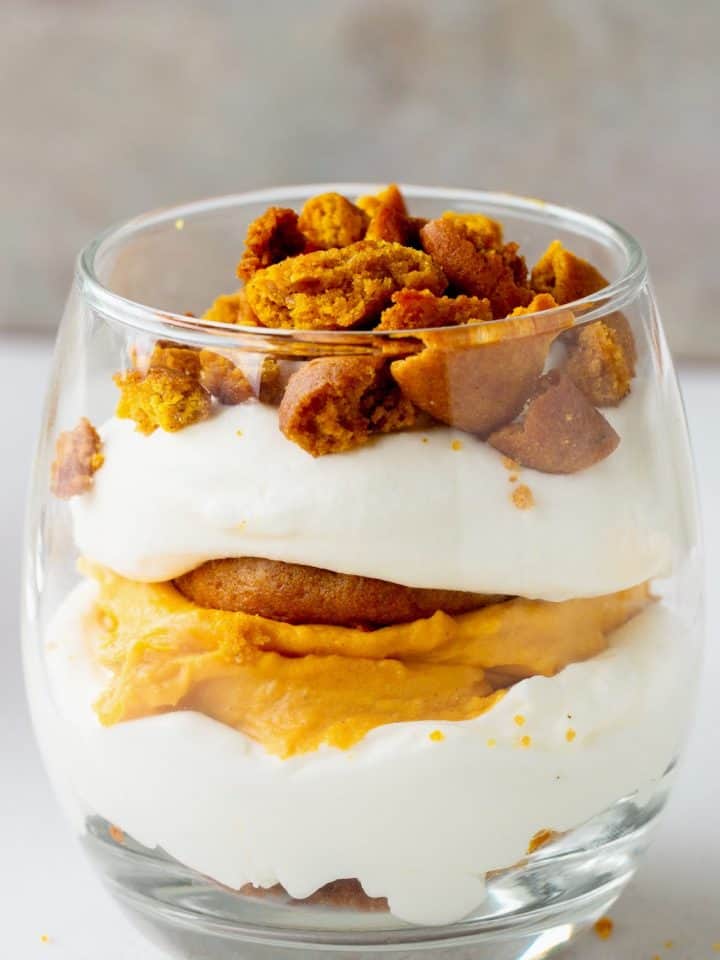 Layered pumpkin cream trifle in a glass on white and grey background.