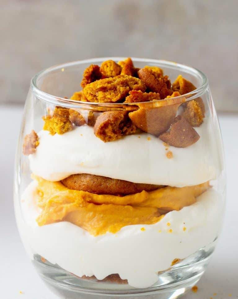 Layered pumpkin cream trifle in a glass on white and grey background.
