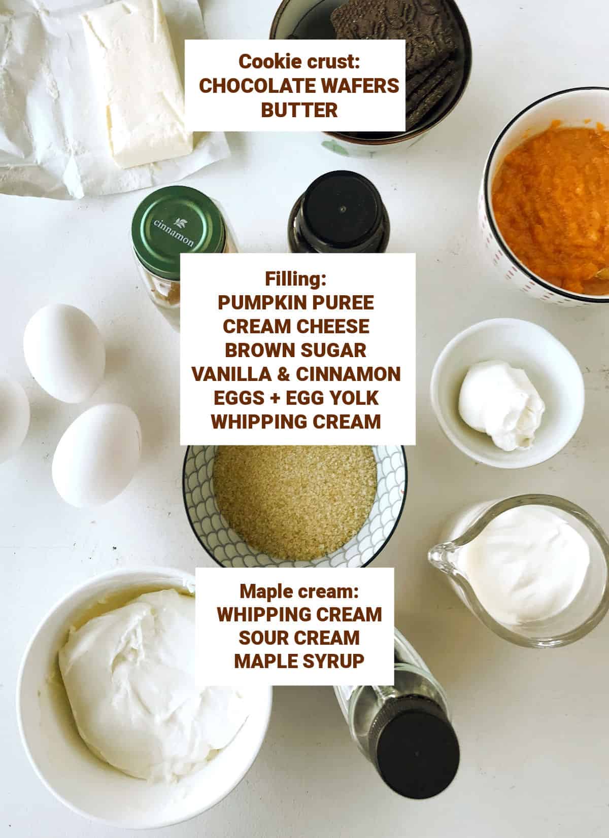 Ingredients for pumpkin maple cream cheesecake in bowls on a white surface including sugar, eggs, cinnamon, vanilla, chocolate crumbs, butter.
