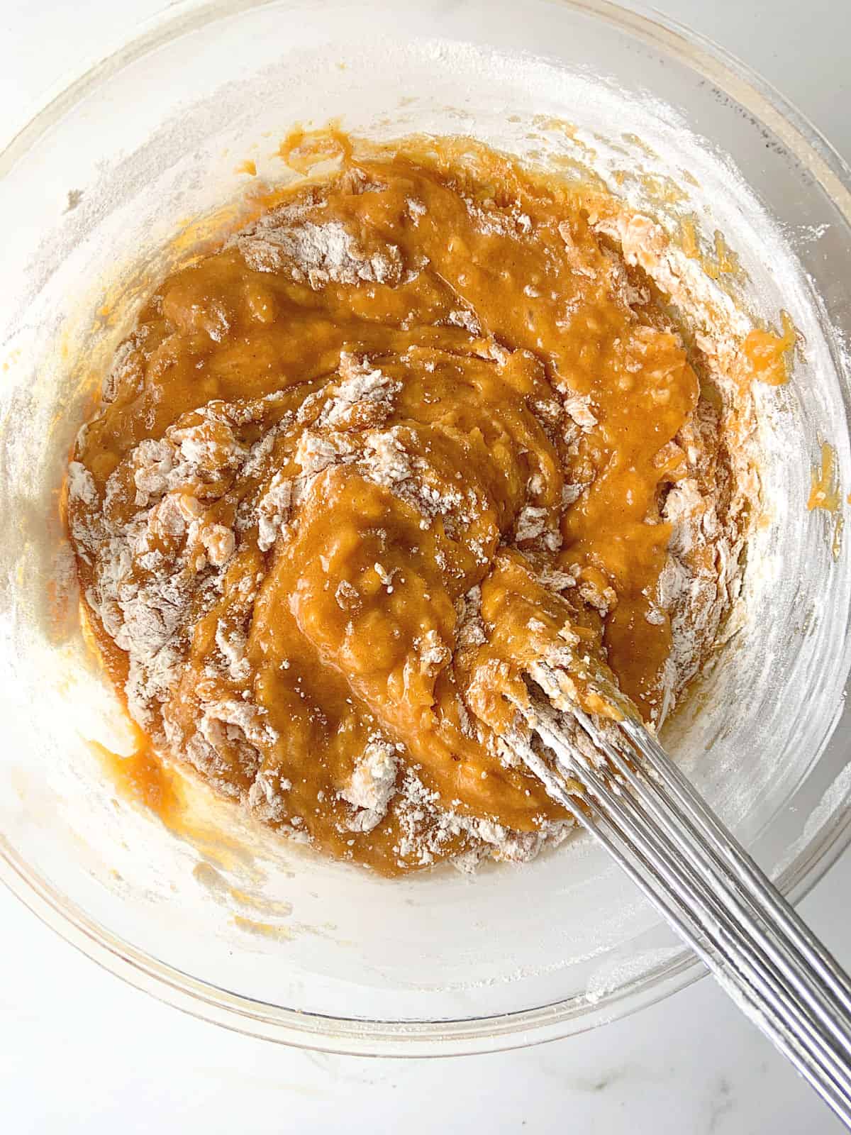 Flour being incorporated in pumpkin batter, metal whisk and glass bowl