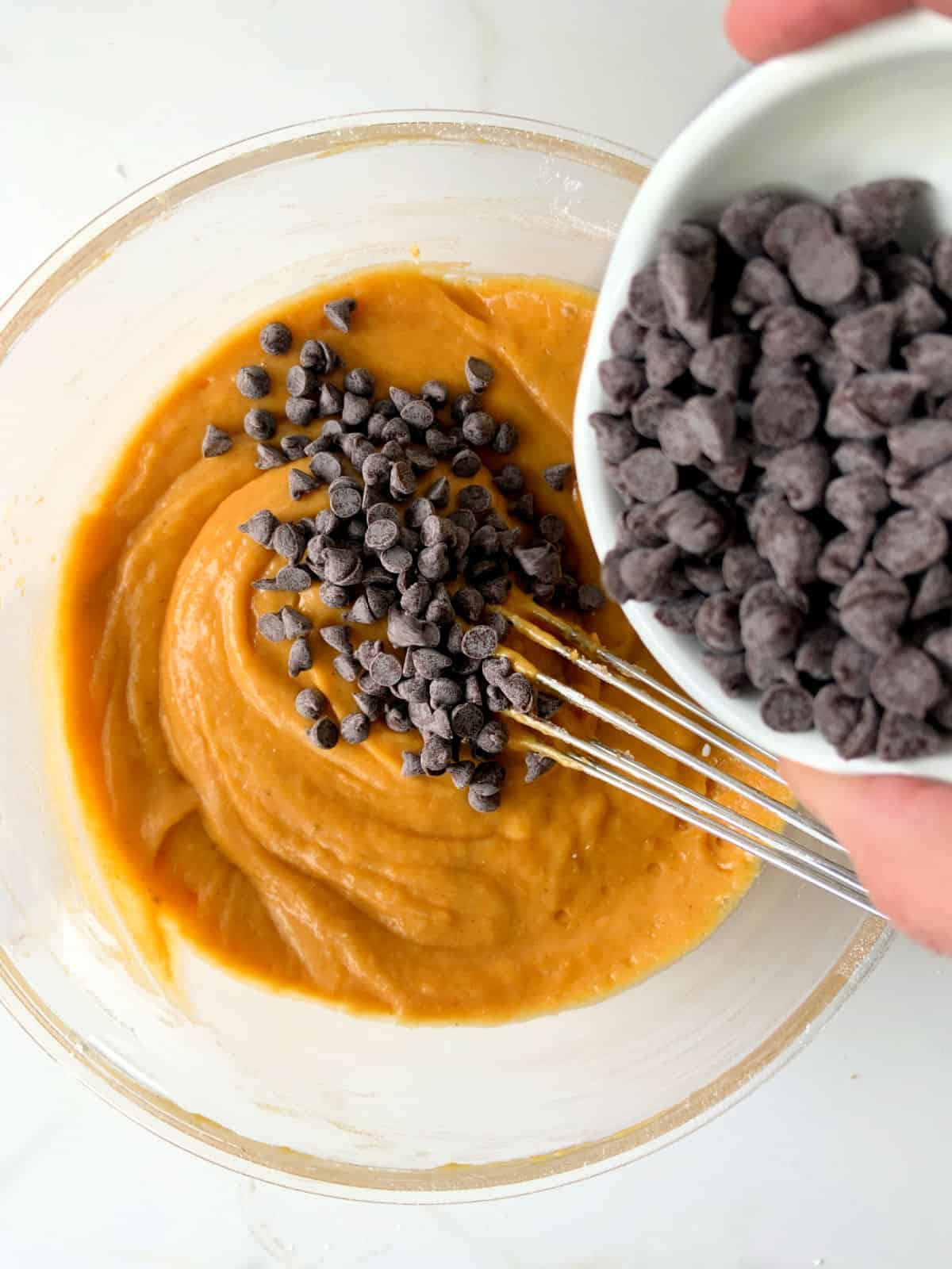 Adding chocolate chips to pumpkin batter in a transparent bowl