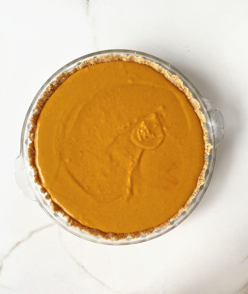 White marble surface with unbaked pumpkin pie on a glass dish.