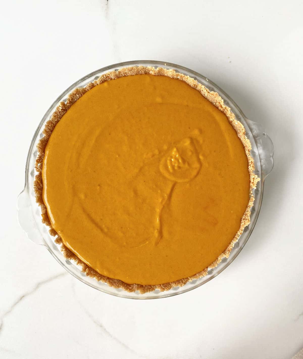 White marble surface with unbaked pumpkin pie on a glass dish. 