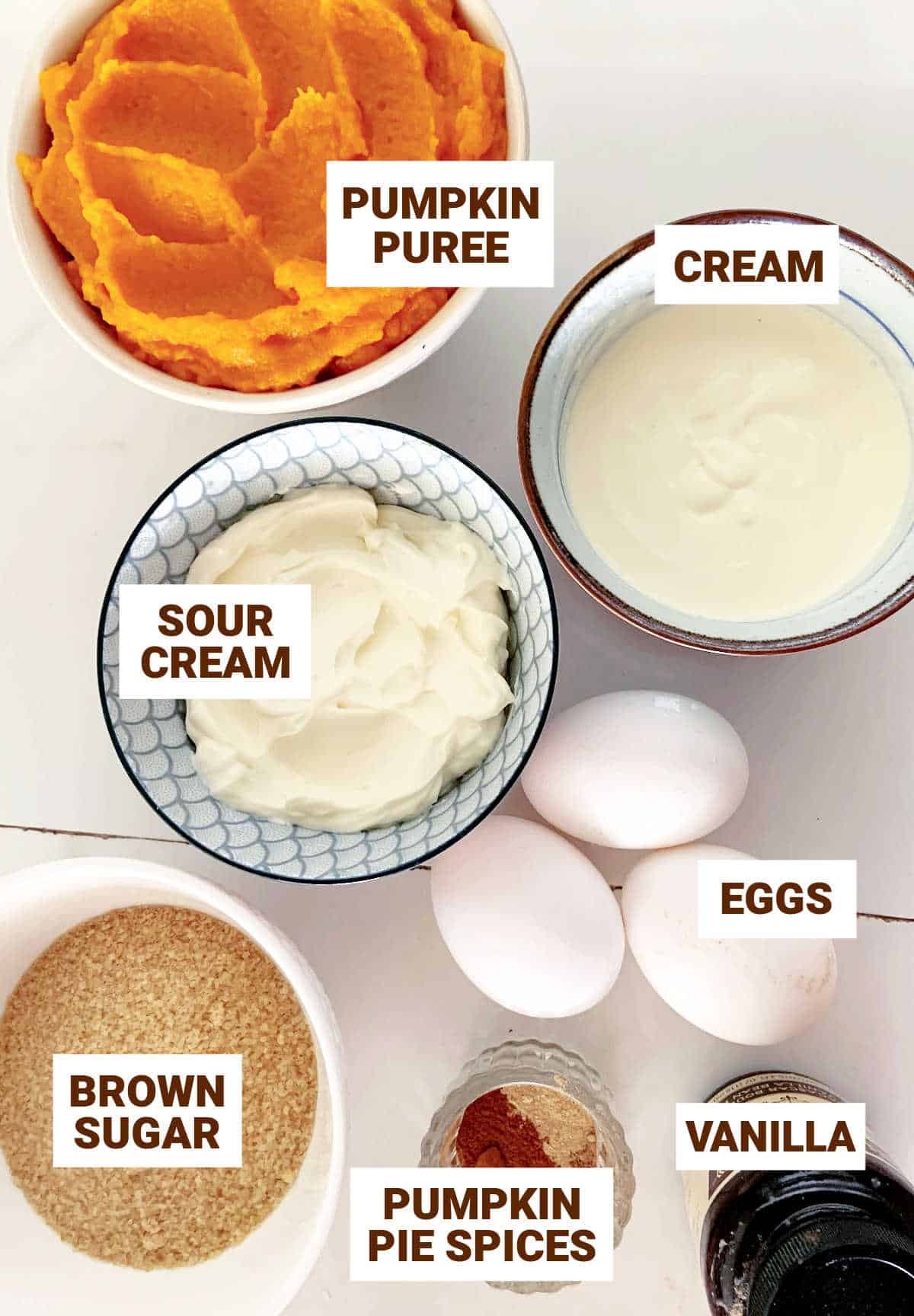 White surface with bowls containing ingredients for pumpkin pie with sour cream and brown sugar.