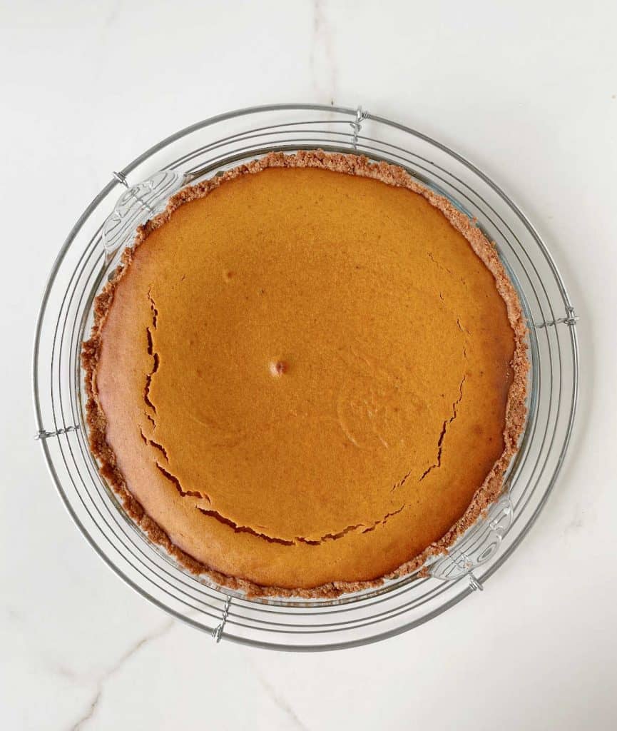 Baked pumpkin pie on a glass plate on a wire rack. Top view on white marble surface.