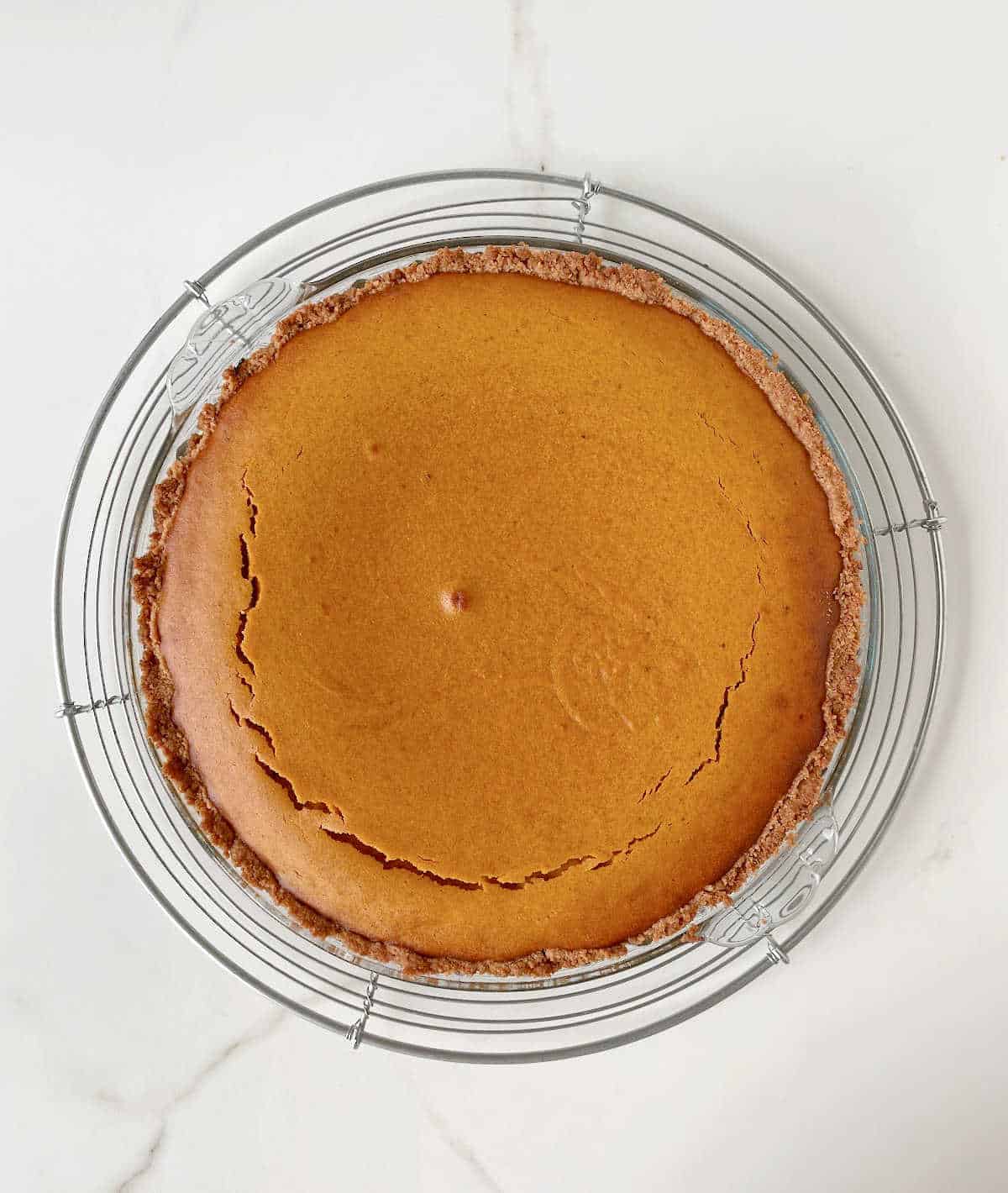Baked pumpkin pie on a glass plate on a wire rack. Top view on white marble surface.