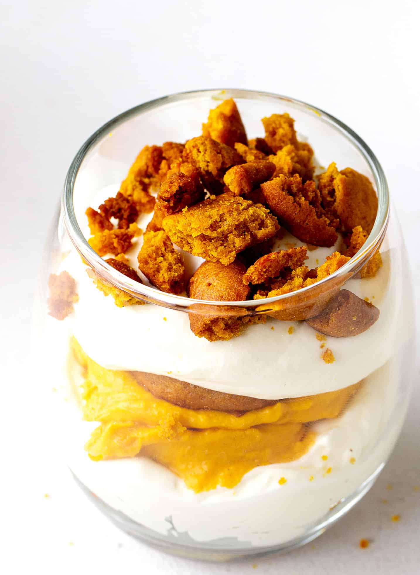 A single glass with pumpkin and cream trifle on a white surface