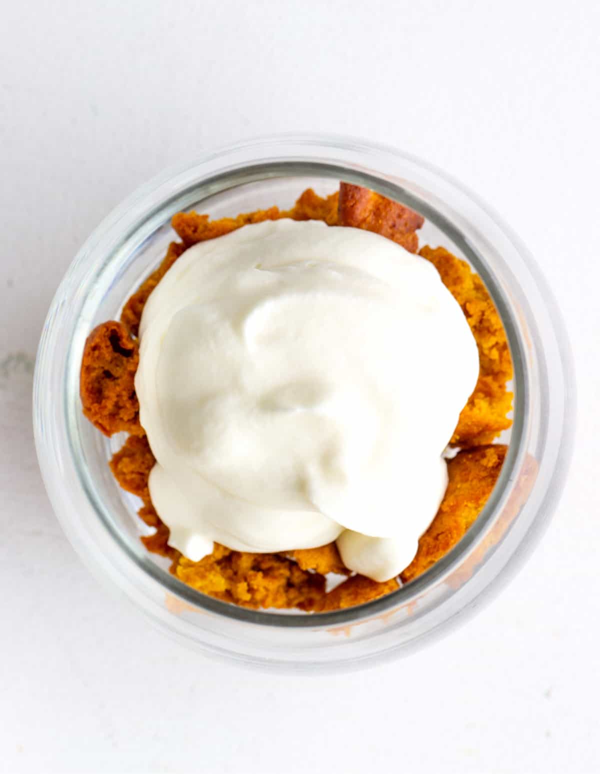 Top view of cream dollop atop pumpkin cake crumbs in a glass 