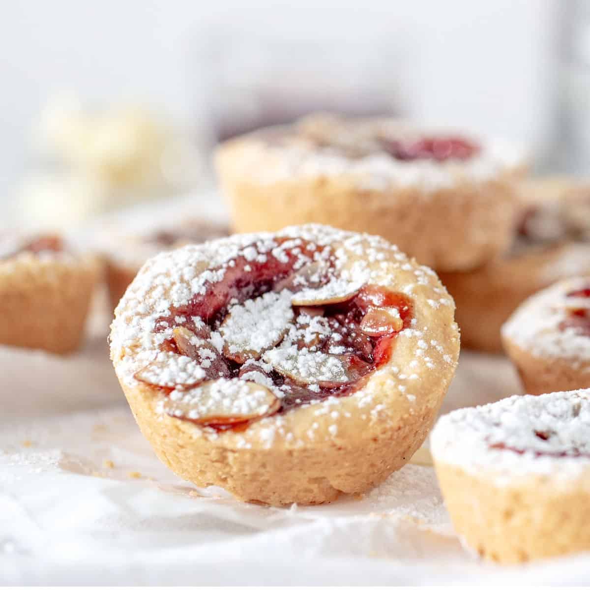 Single raspberry jam tart with almonds and powdered sugar among more blurred ones.