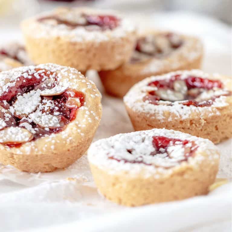 Mini shortbread raspberry jam cakes on a white cloth, sprinkled with powdered sugar.