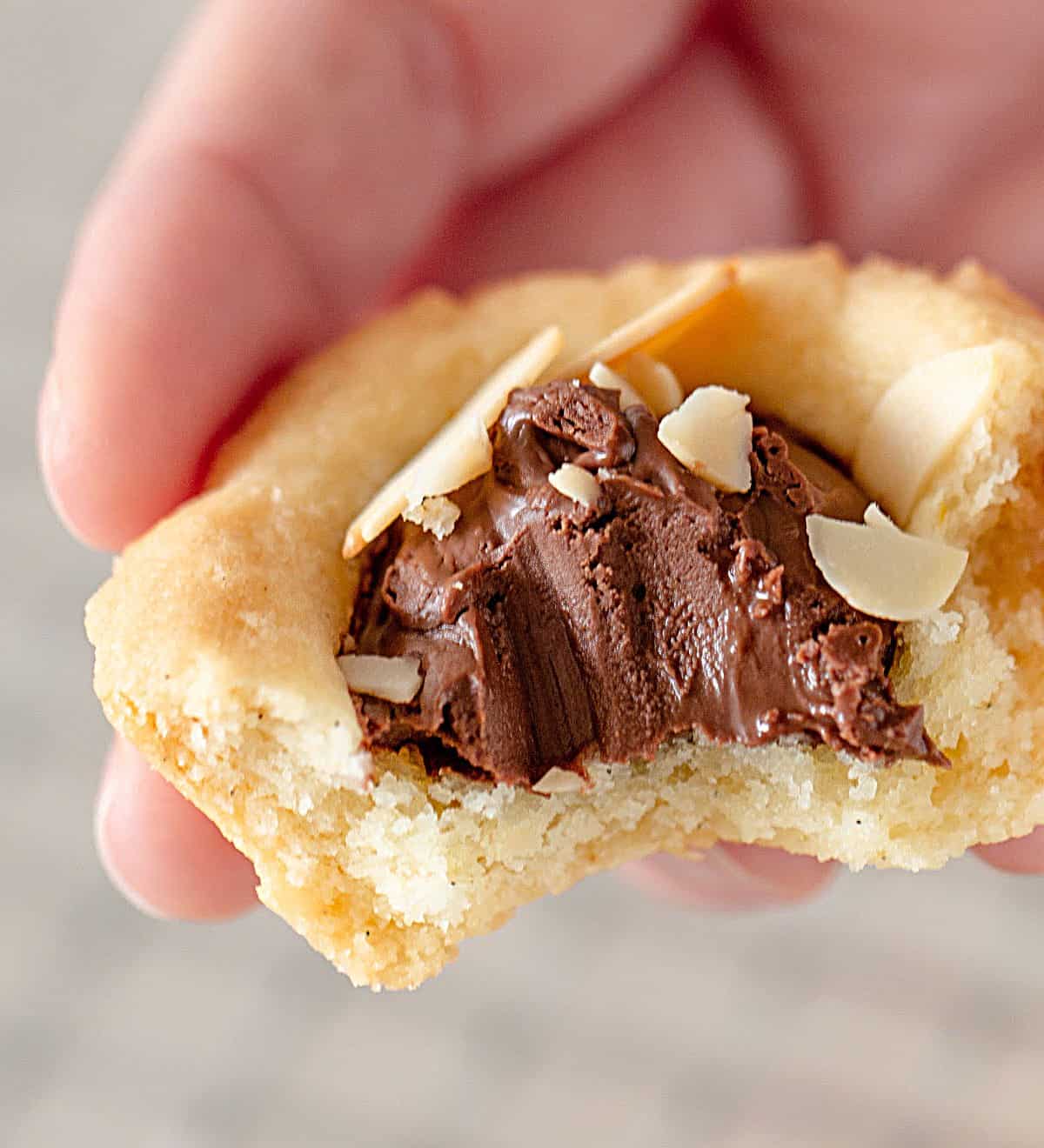 Hand holding bitten shortbread mini tart filled with nutella. 