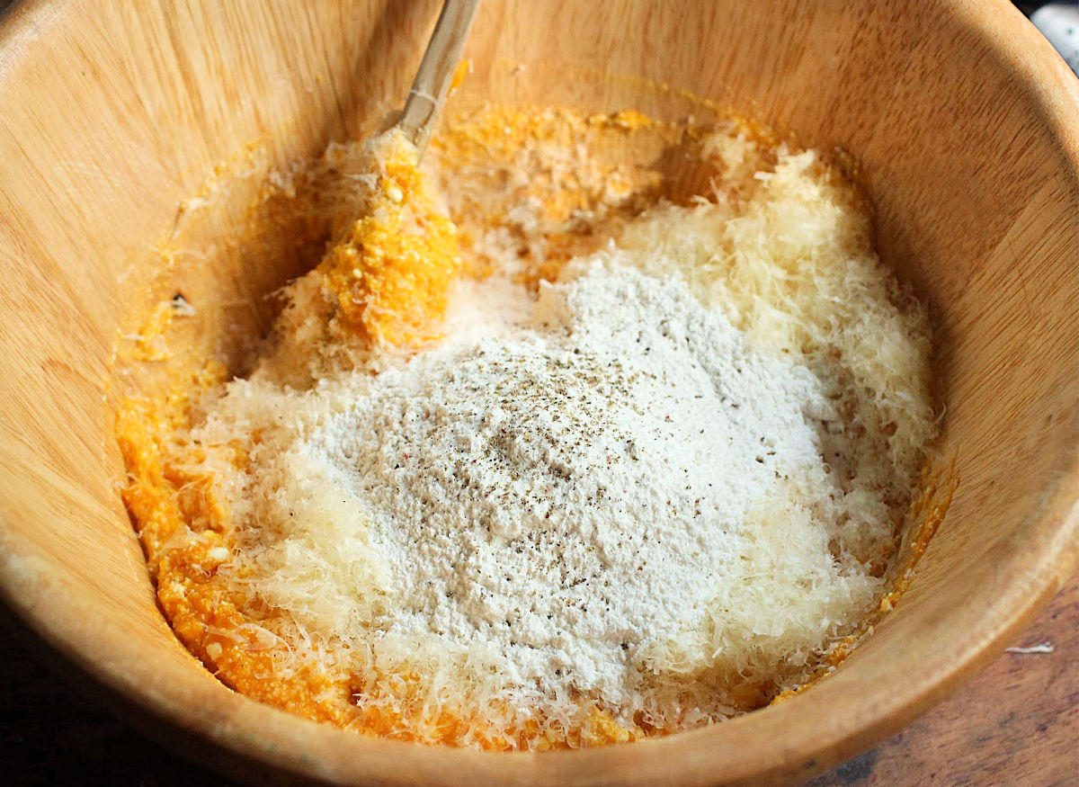 Flour and pepper added to pumpkin gnocchi mixture in a light wood bowl