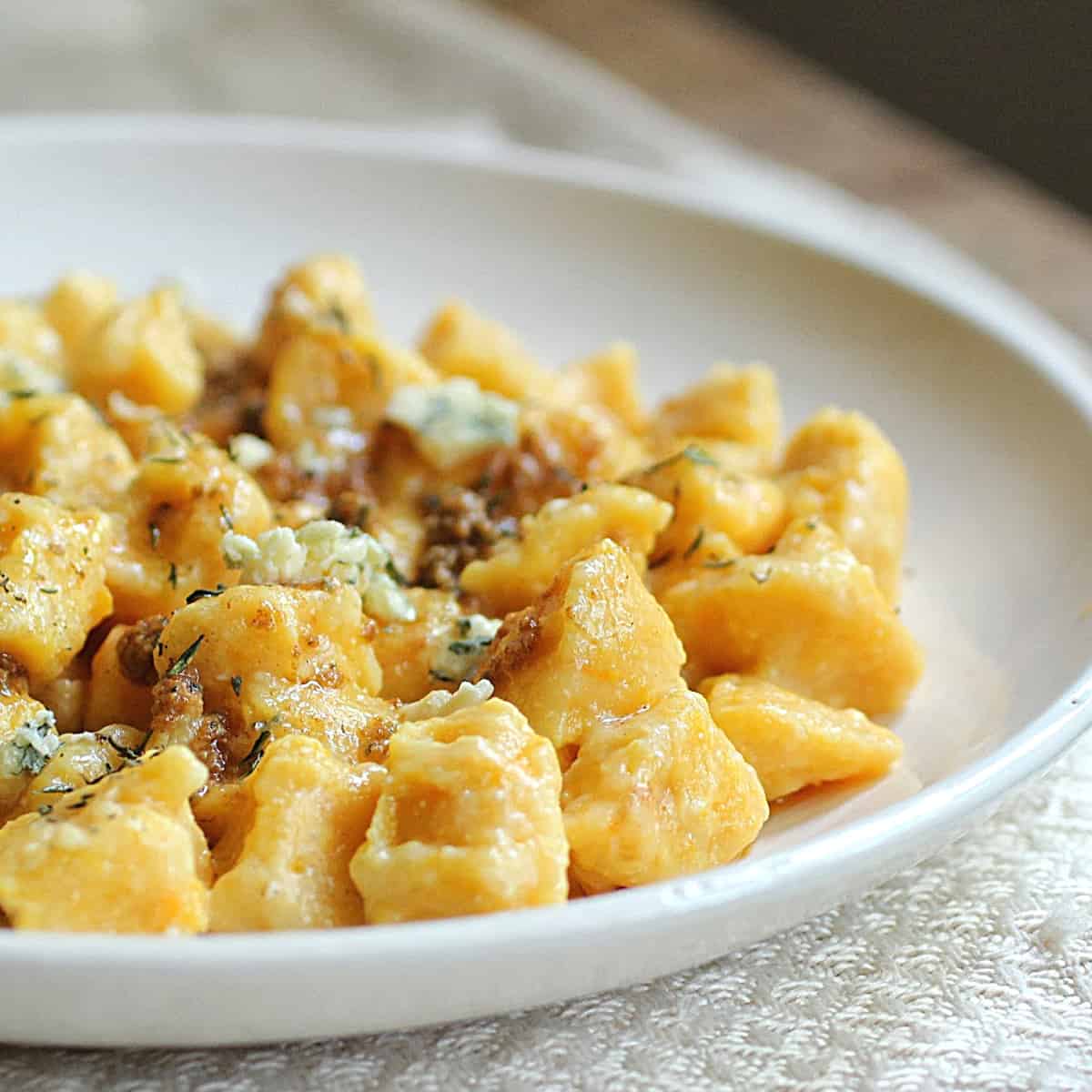 White round plate with pumpkin gnocchi on a white cloth