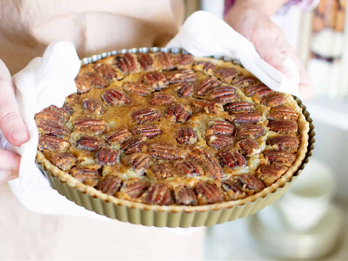 Holding tart pan with baked pecan pie and a white kitchen towel.