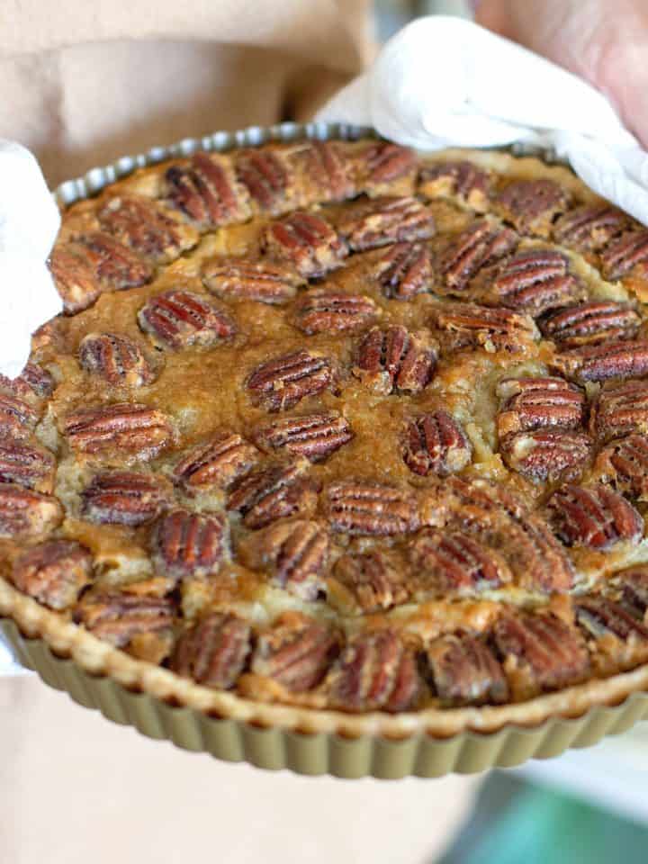 Hands holding pan with pecan pie with white kitchen towel
