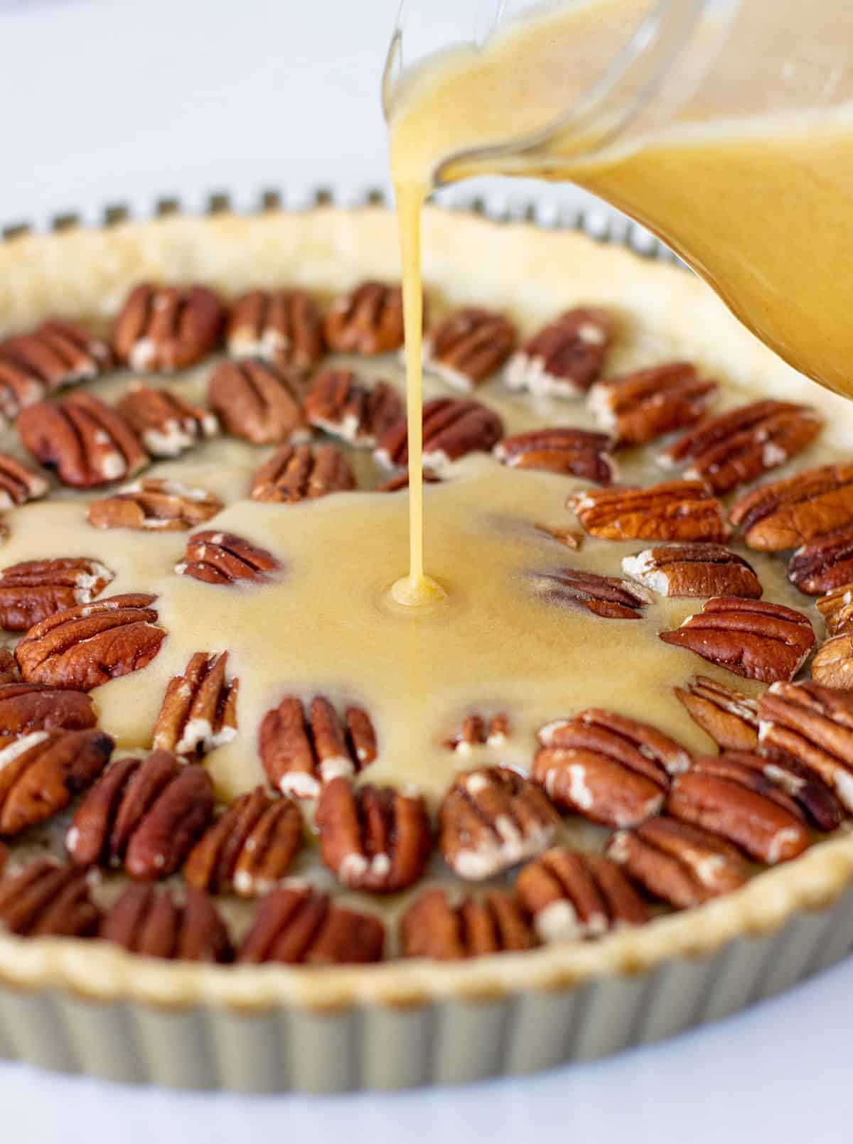 Bourbon butter filling being poured in a pie crust filled with pecans.
