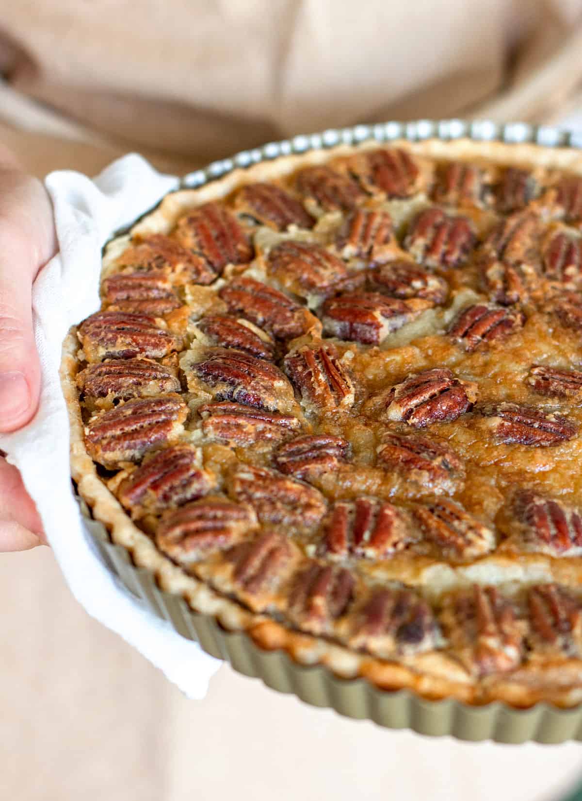 Partial view of hands holding pecan pie with a white kitchen towel.