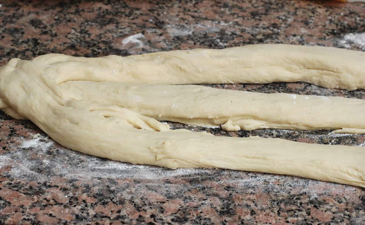 Three ropes of dough on a brown marble counter about to be braided