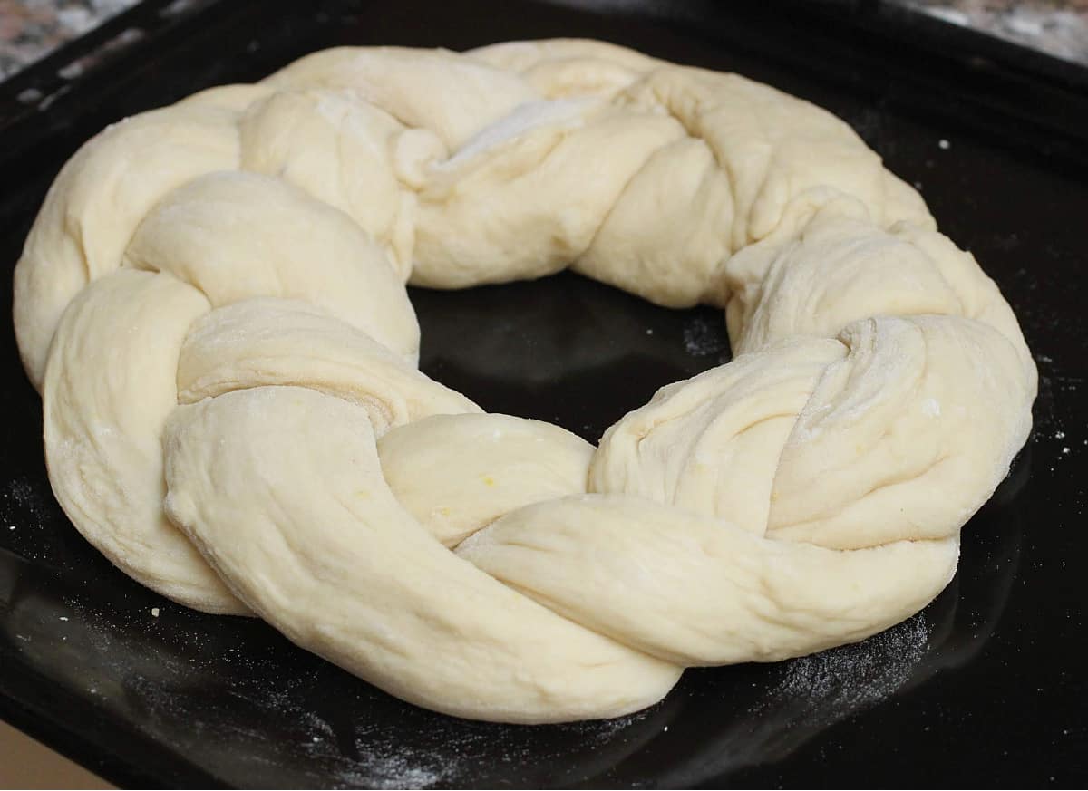 Braided round unbaked bread on a black oven sheet