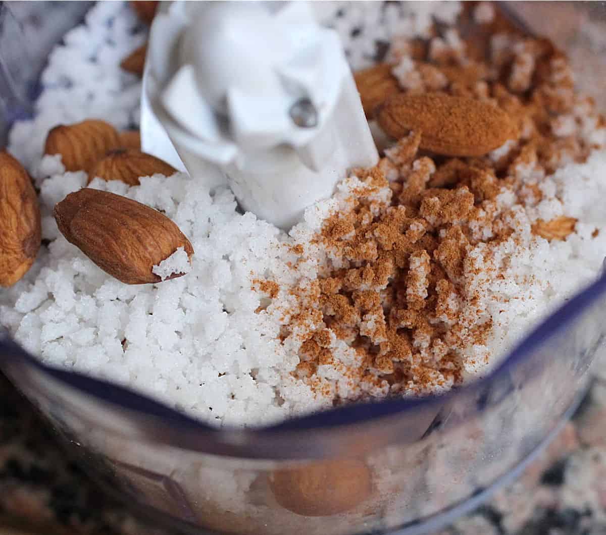 Top view of coarse pearl sugar, cinnamon and almonds in food processor bowl