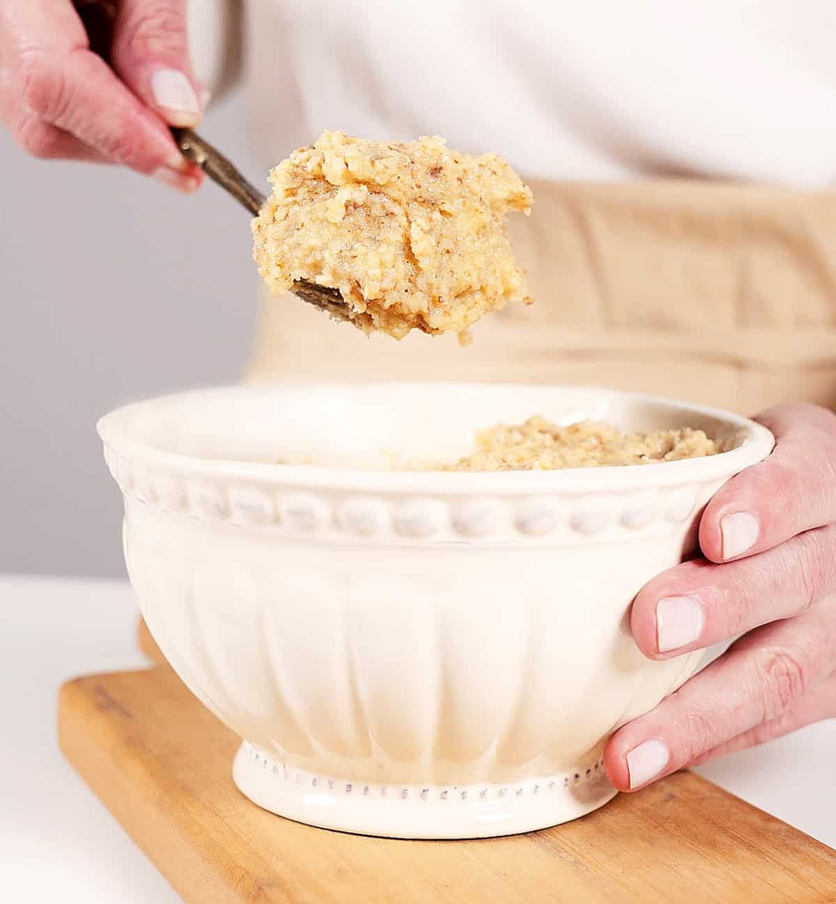Partial view of person scooping frangipane from a cream colored bowl on a wooden board. 
