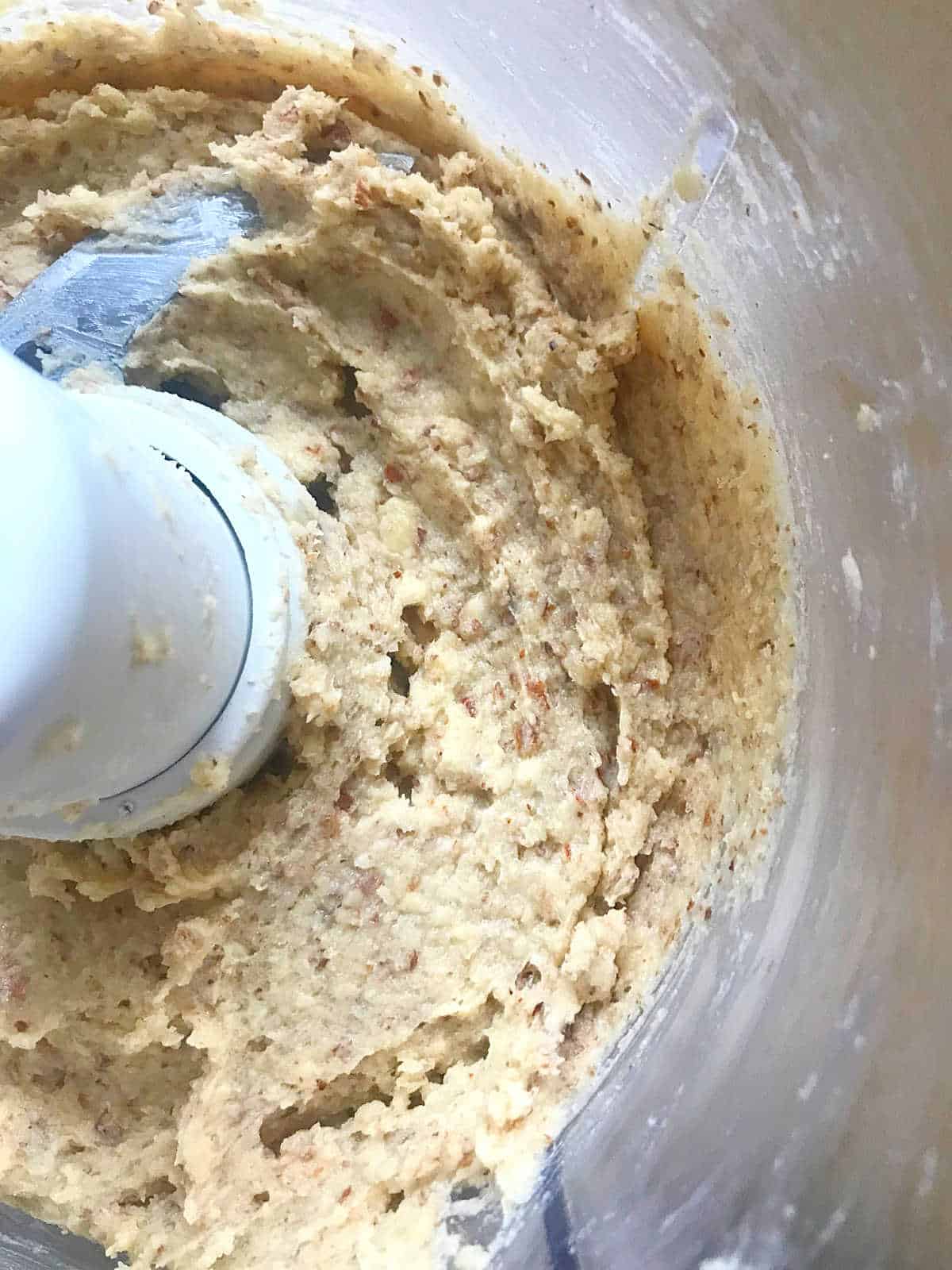 Almond cream in the bowl of a food processor seen from the top. 
