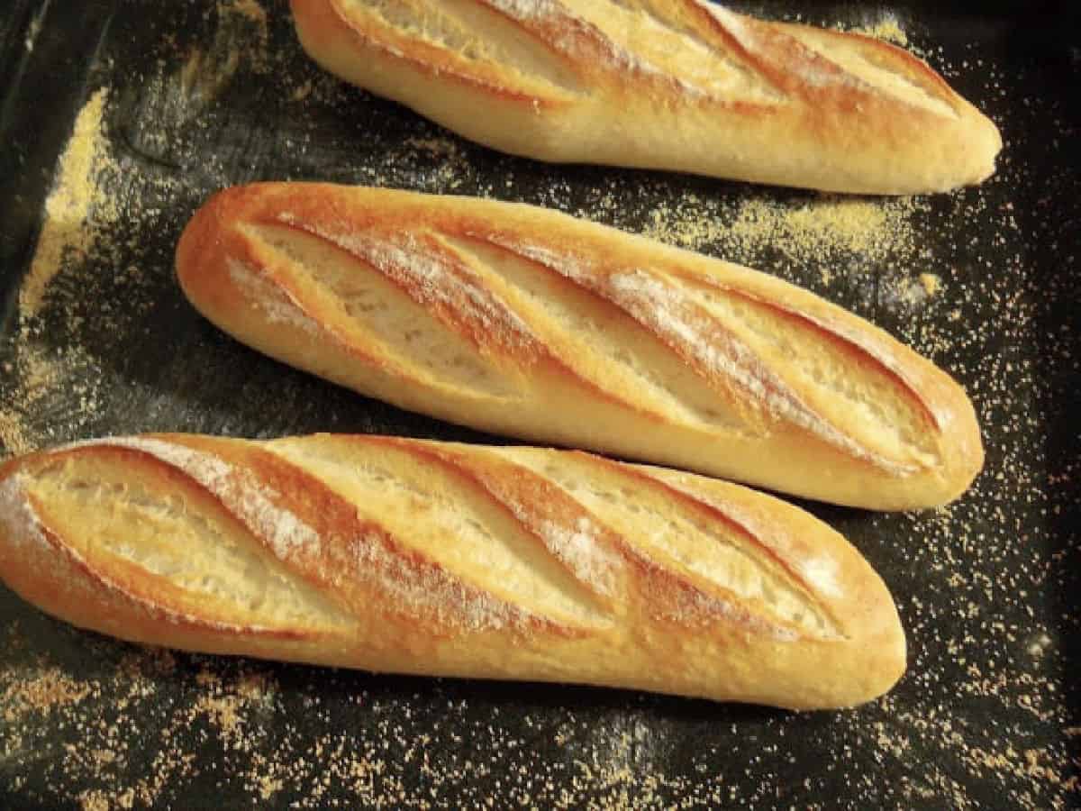 Golden homemade French baguettes on a dark baking tray. 