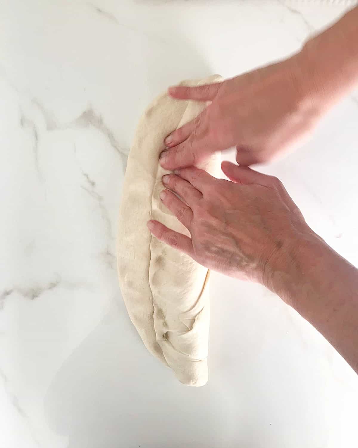 Hands forming a baguette on a white marble surface.