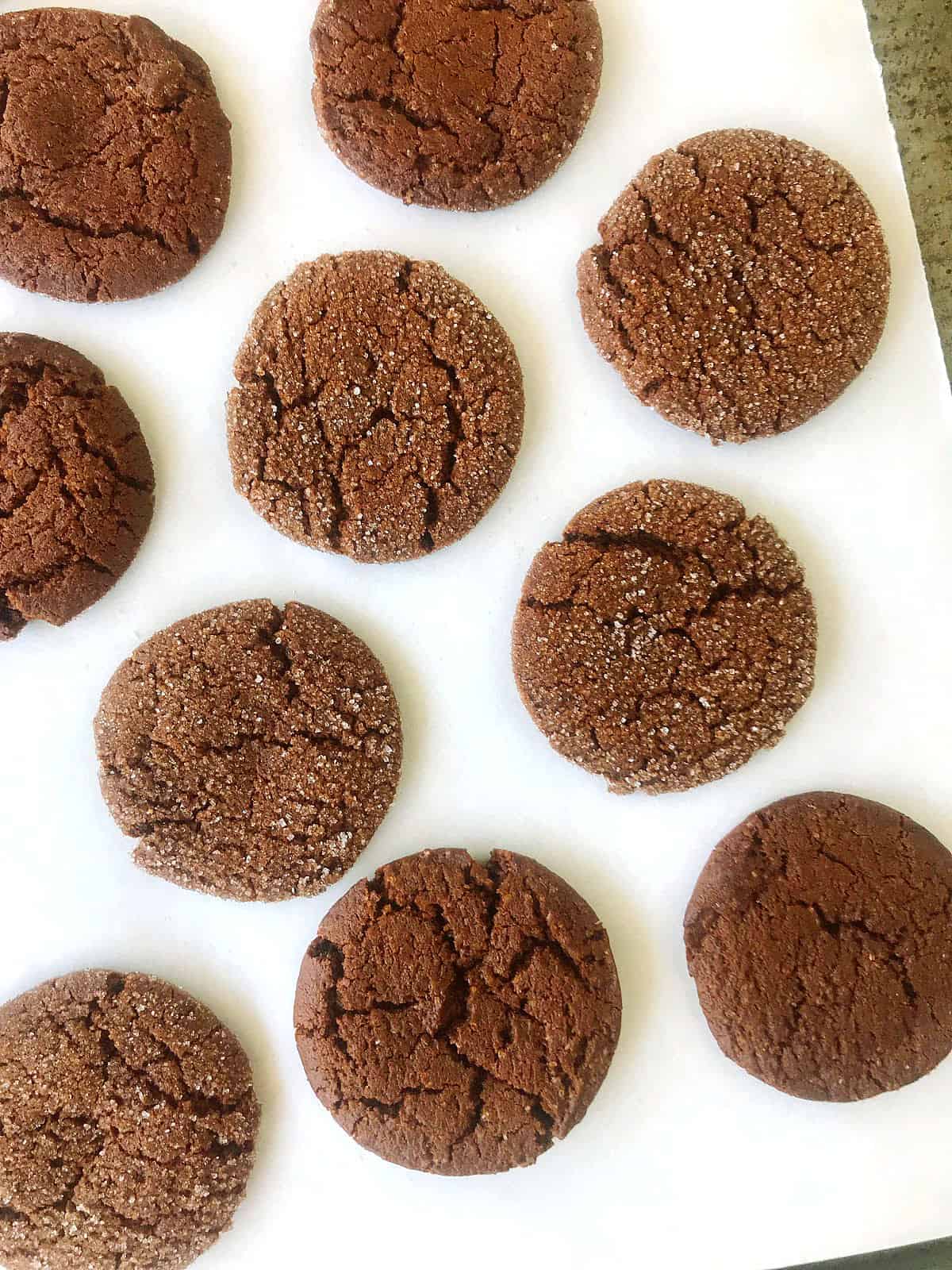 Flat view of dark cracked molasses cookies on white parchment paper.