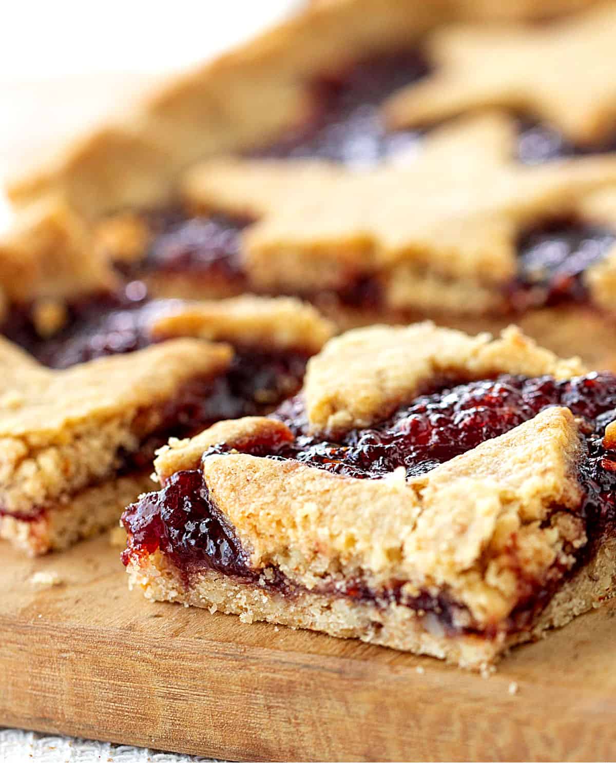 Squares of raspberry linzer torte on light colored wooden board.