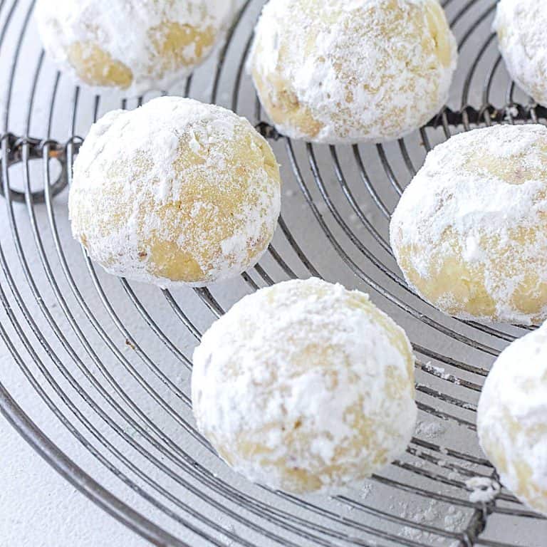Several snowball cookies on a wire rack placed over a white surface.