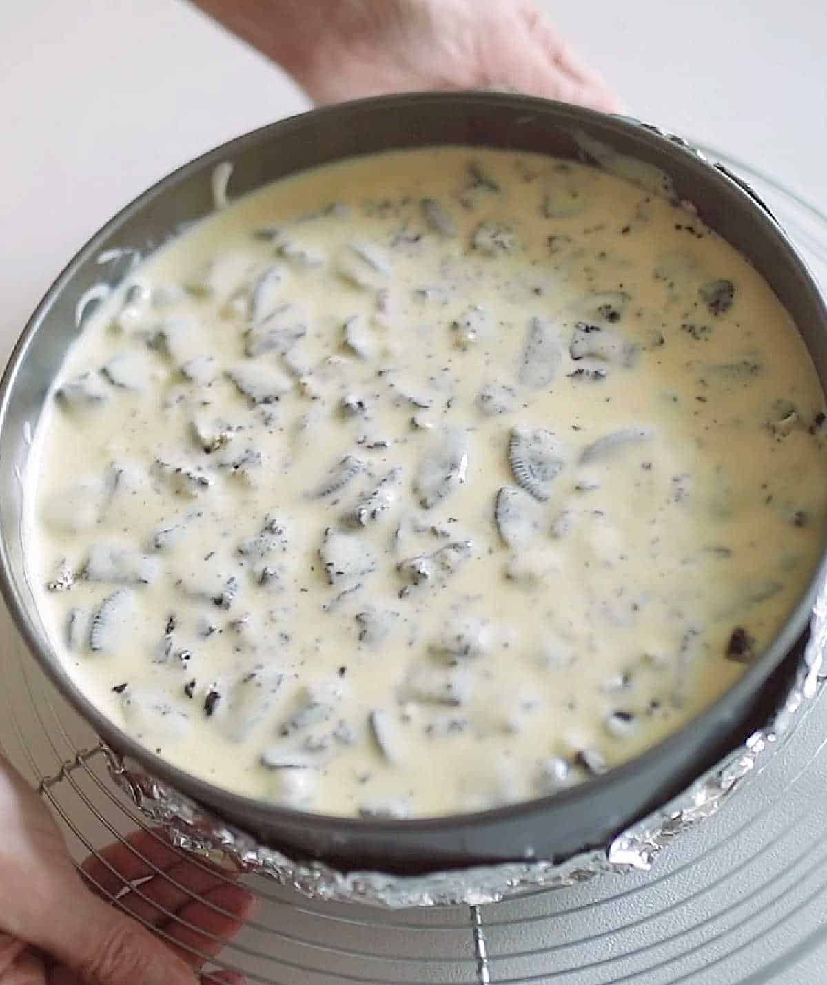Close up of cookies and cream cheesecake in a round pan before baking.