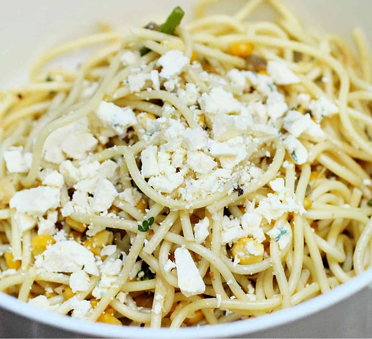 Spaghetti with cheese pieces in a white plastic bowl
