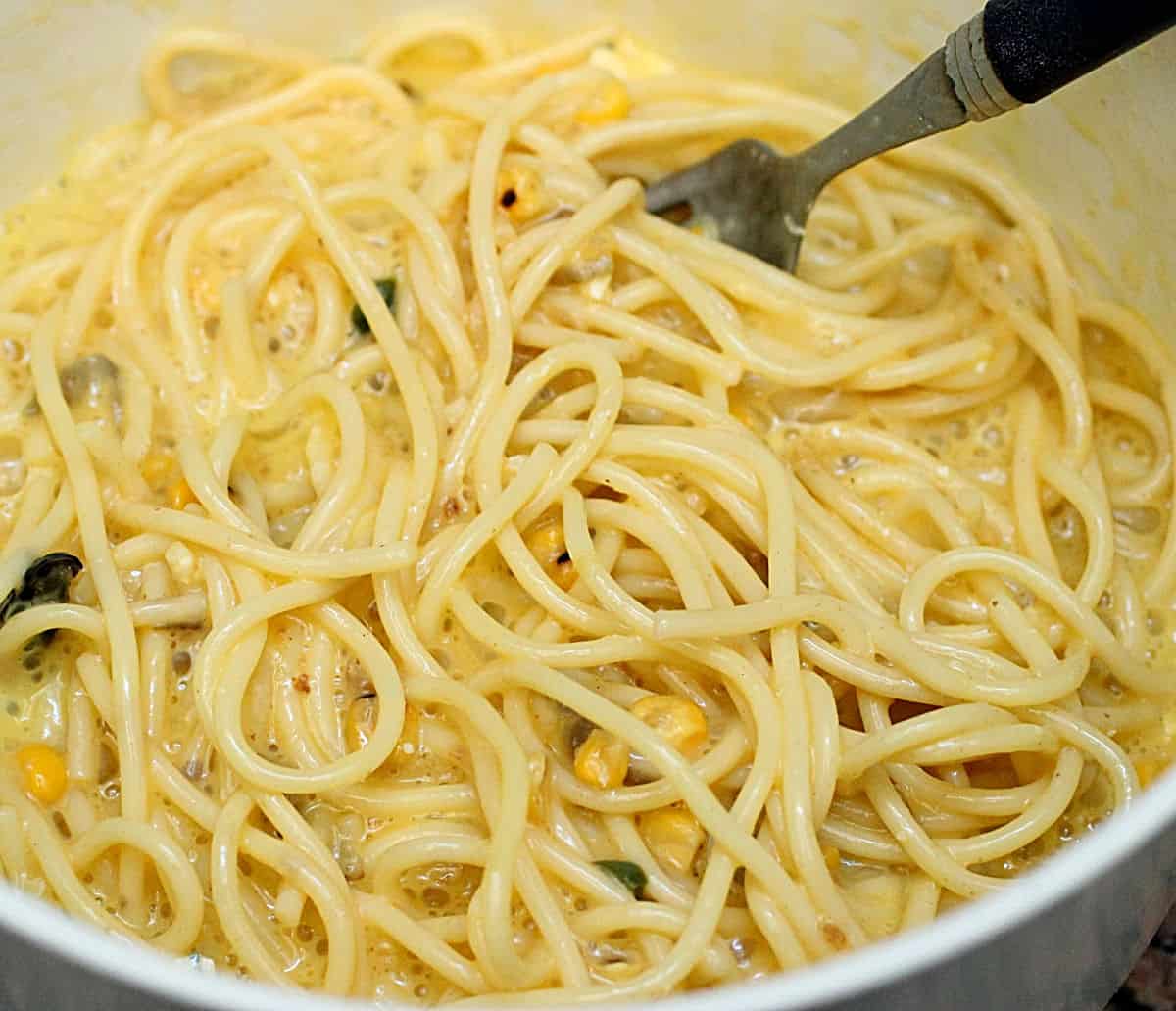 Close up of cooked spaghetti with raw eggs, corn, parsley and a fork