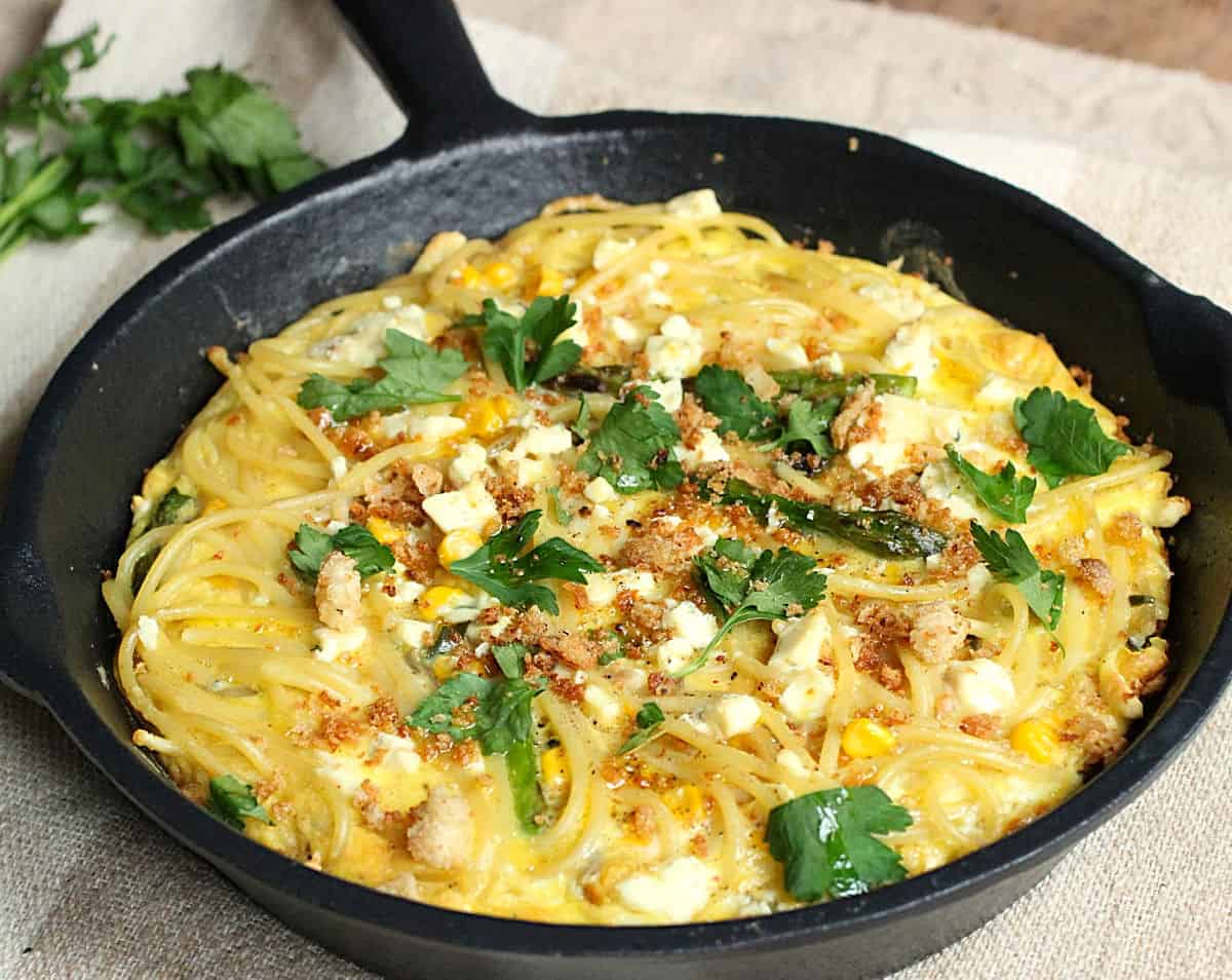 Frittata of pasta in cast iron skillet on beige cloth.