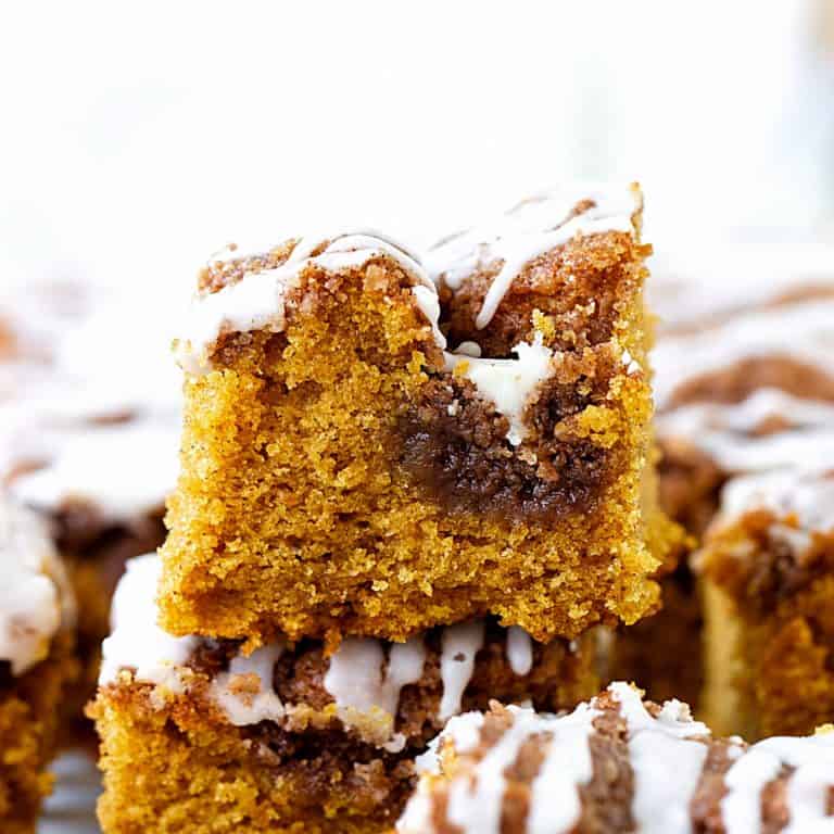 Square of iced pumpkin crumble cake on top of others, white background