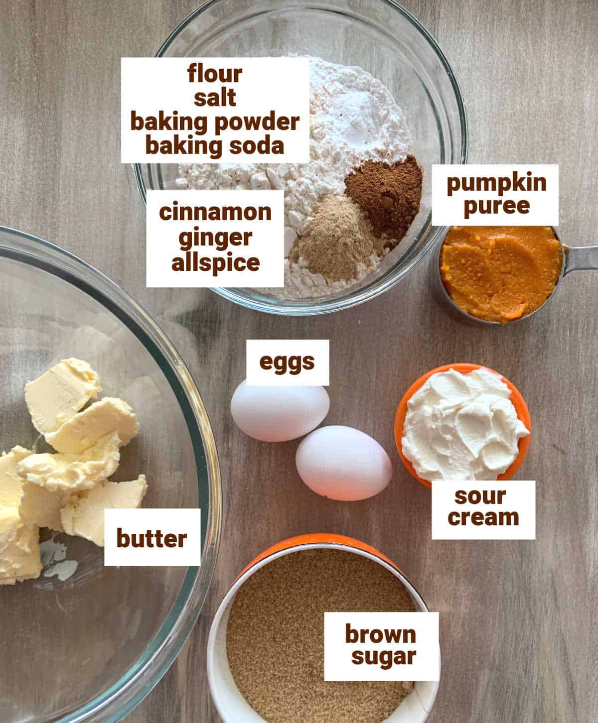 Brownish surface with bowls containing pumpkin cake ingredients, two whole eggs