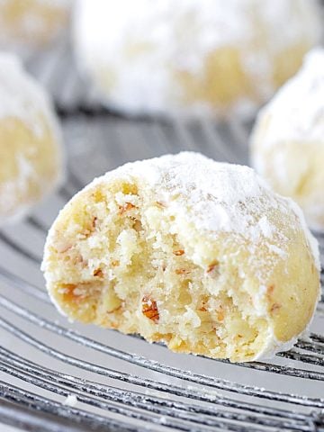 Bitten snowball cookie on a wire rack with whole ones in the background.