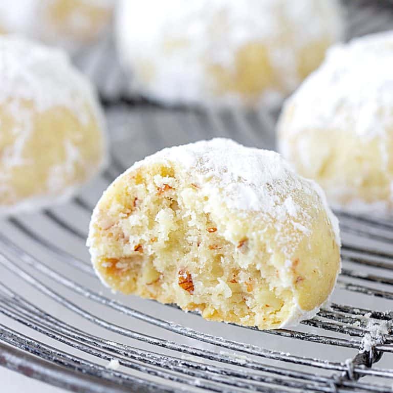 Bitten snowball cookie on a wire rack with whole ones in the background.