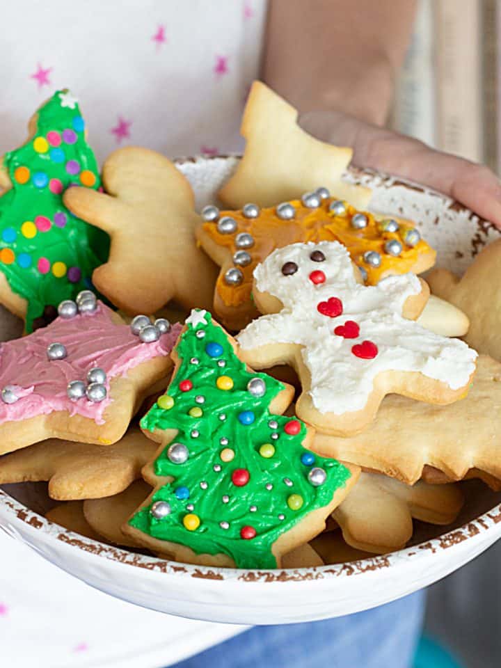 Holding white plate with frosted Christmas sugar cookies