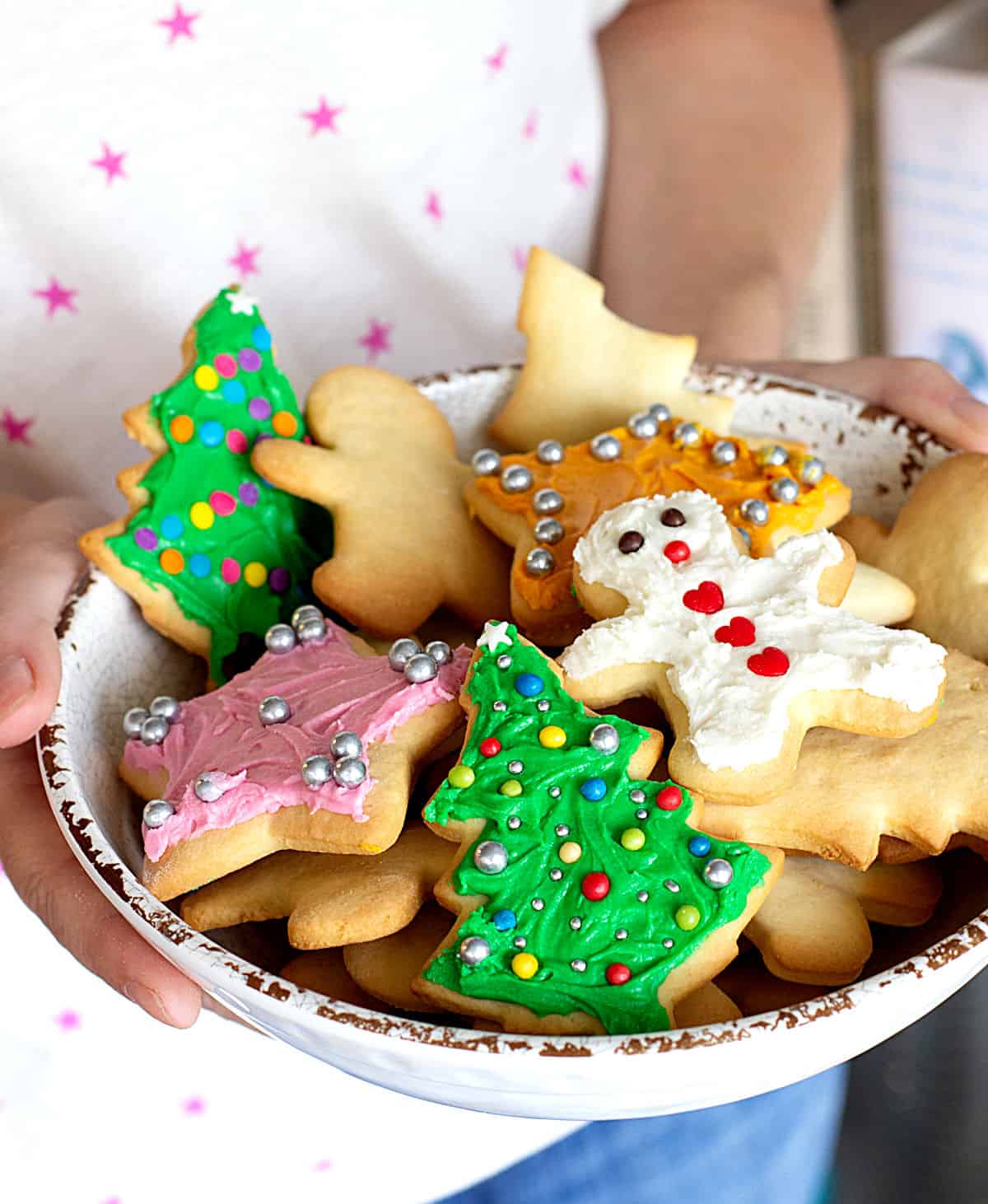 Person holding white shallow bowl with different frosted colorful Christmas cut out cookies