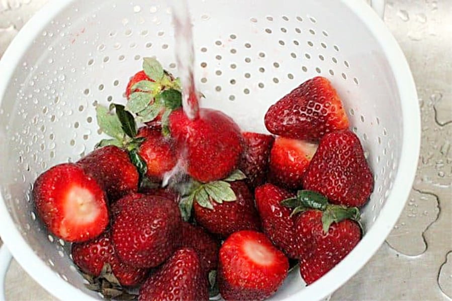 Rinsing whole strawberries in a white colander under the sink tap