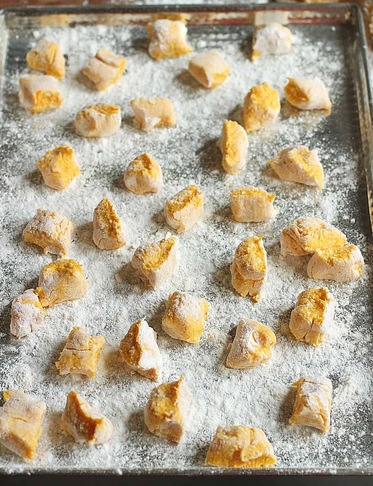 A metal tray with flour and single rows of pumpkin gnocchi